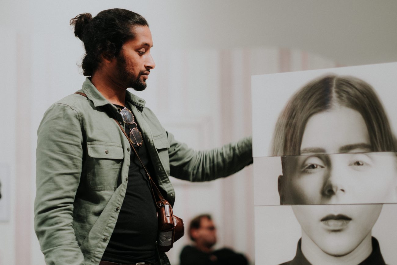 Ein Mann mit Bart und Zopf neben einer Fotoinstallation