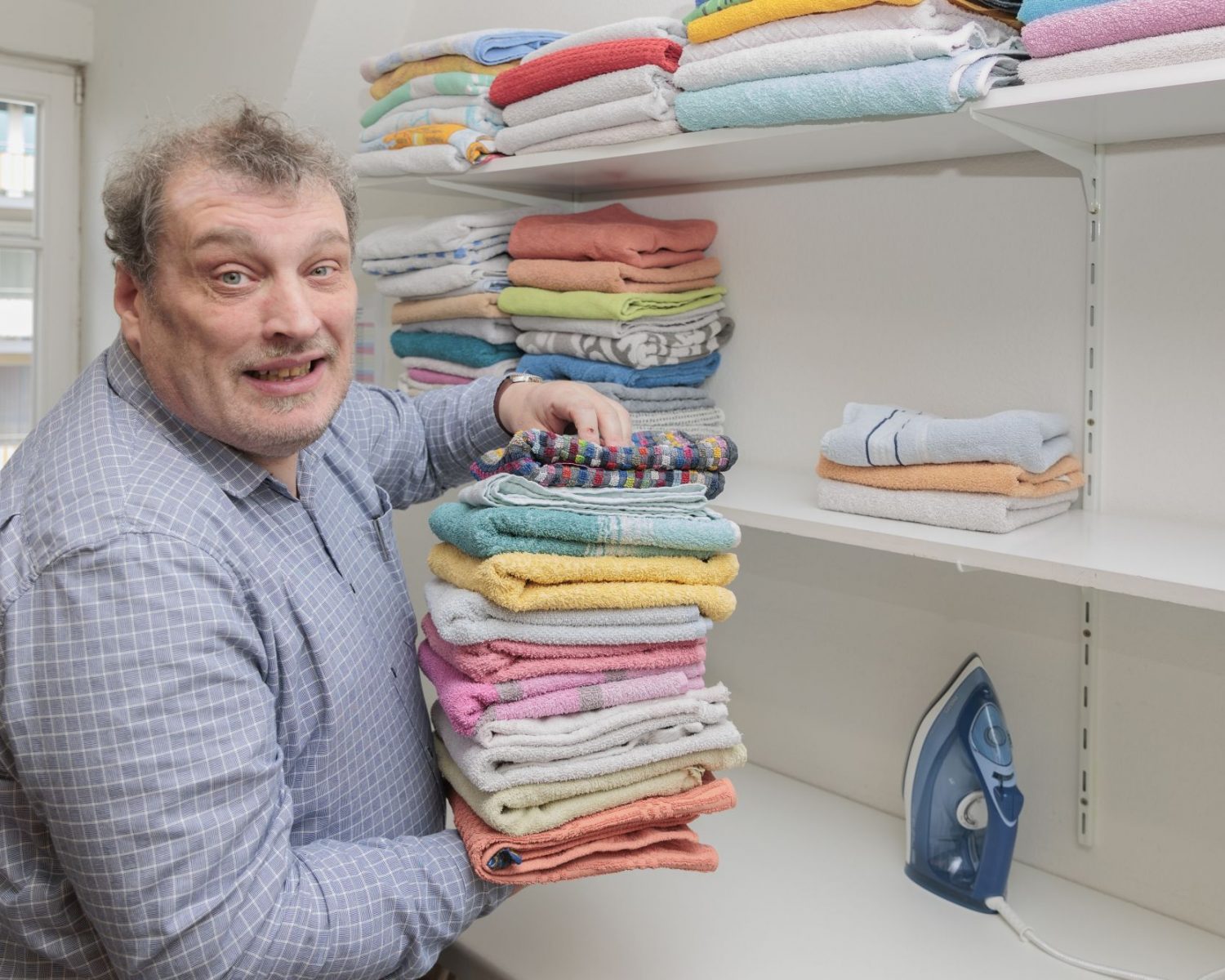 Mann sortiert einen bunten Stapel Handtücher in ein Regal.